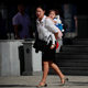 A woman carries her daughter as she waits to cross a street.
